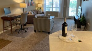 Ein modernes Wohnzimmer mit Schreibtisch, Sofa, einem gestreiften Sessel, Couchtisch und Essbereich, inklusive Weinflasche und Gläsern.