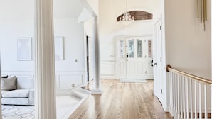 A spacious hallway with a wooden floor, white walls, and a chandelier. - Coastal Haven Seaside Serenity Retreat (Federal Way)