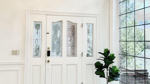 A spacious entryway with a large arched window, a white door with glass panels, a chandelier, and a potted plant. - Coastal Haven Seaside Serenity Retreat (Federal Way)