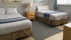 A hotel room with two beds, a nightstand, a lamp, and two beach-themed paintings on the wall. - The Old Man the Sea-seaview 101 (Madeira Beach)
