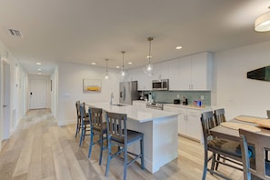 A modern kitchen with white cabinetry, a central island with bar stools, and pendant lighting.