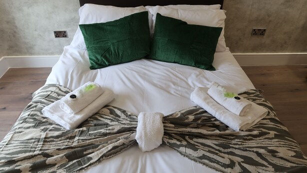 A neatly made bed with white linens, two green pillows, and two towels folded on the bed. - Casa Bella in Sherborne s Historic Quarter (Sherborne)