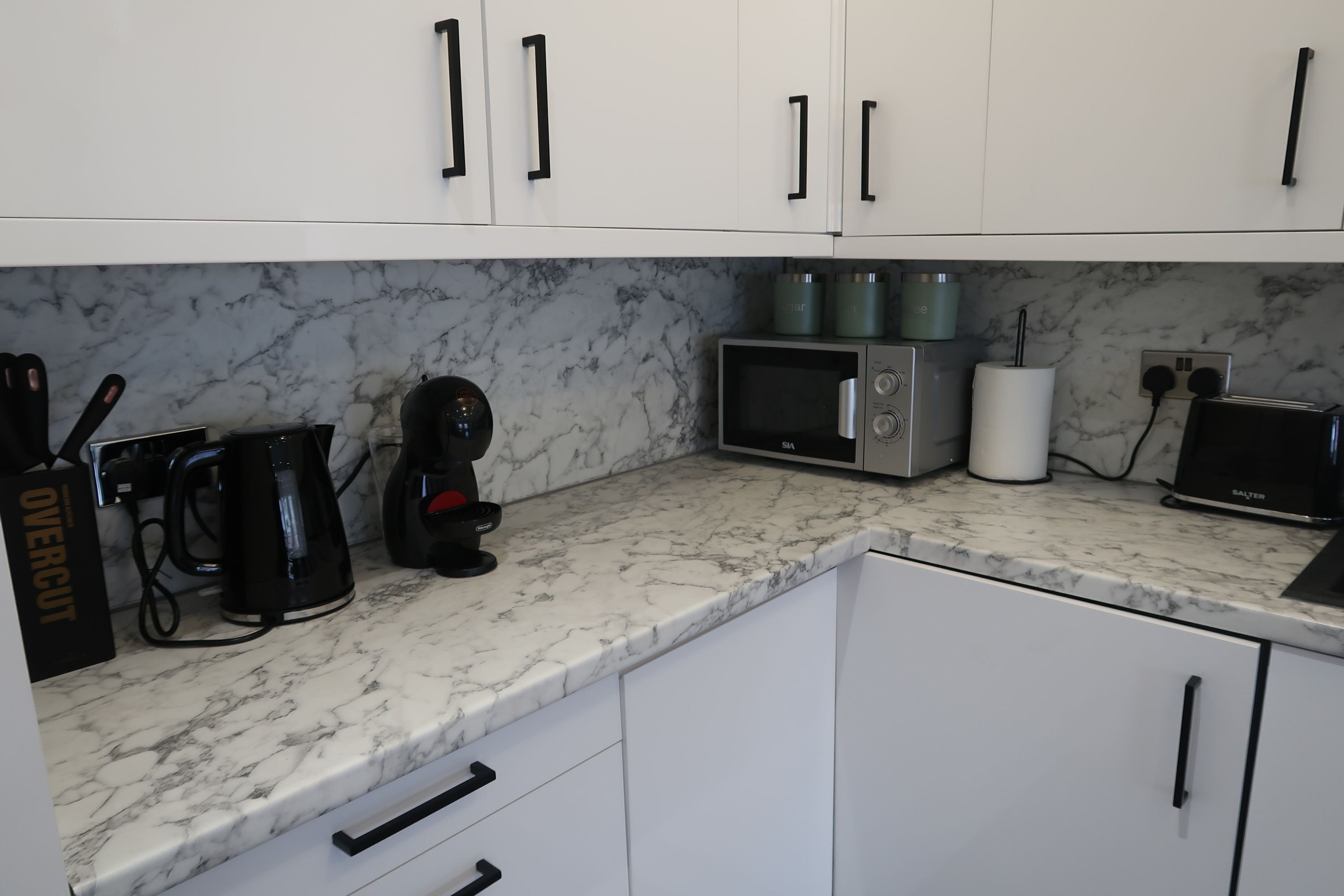 A kitchen with white cabinets, a marble countertop, a coffee maker, a microwave, a toaster, and a kettle.