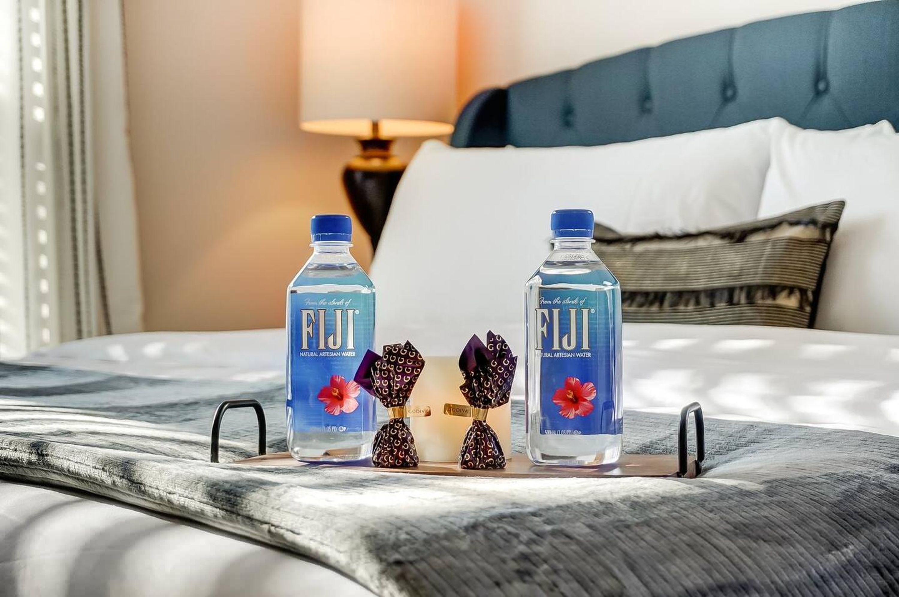 A bed with two Fiji water bottles and decorative items on a tray.