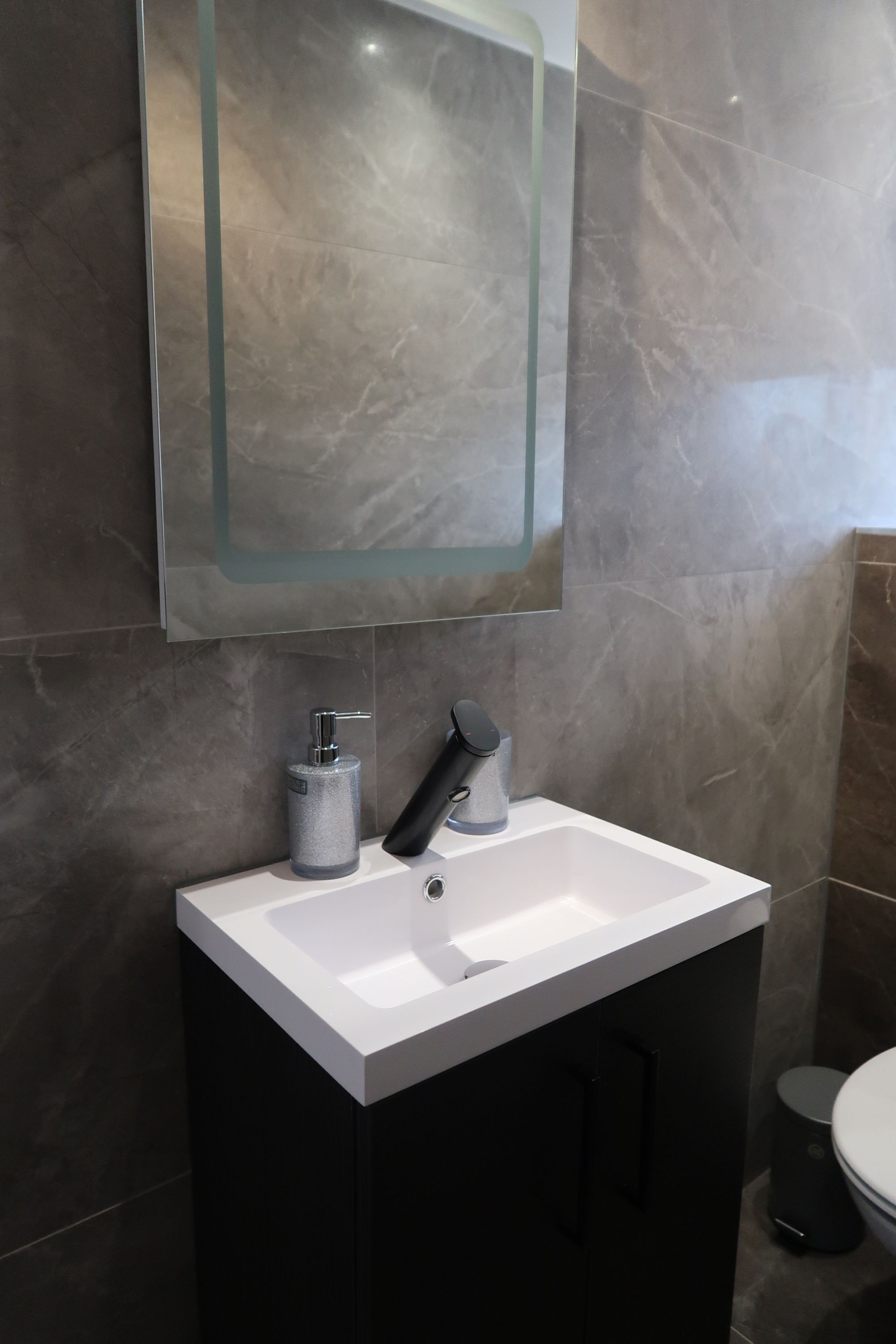 A modern bathroom with a white sink, dark cabinets, a glass-encased mirror, and a toilet.