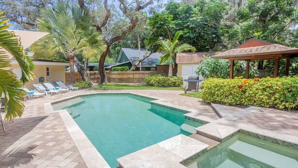 A rectangular swimming pool with a tiled deck, surrounded by palm trees and a gazebo. - Breathless Backyard Amazing Pool (Largo)