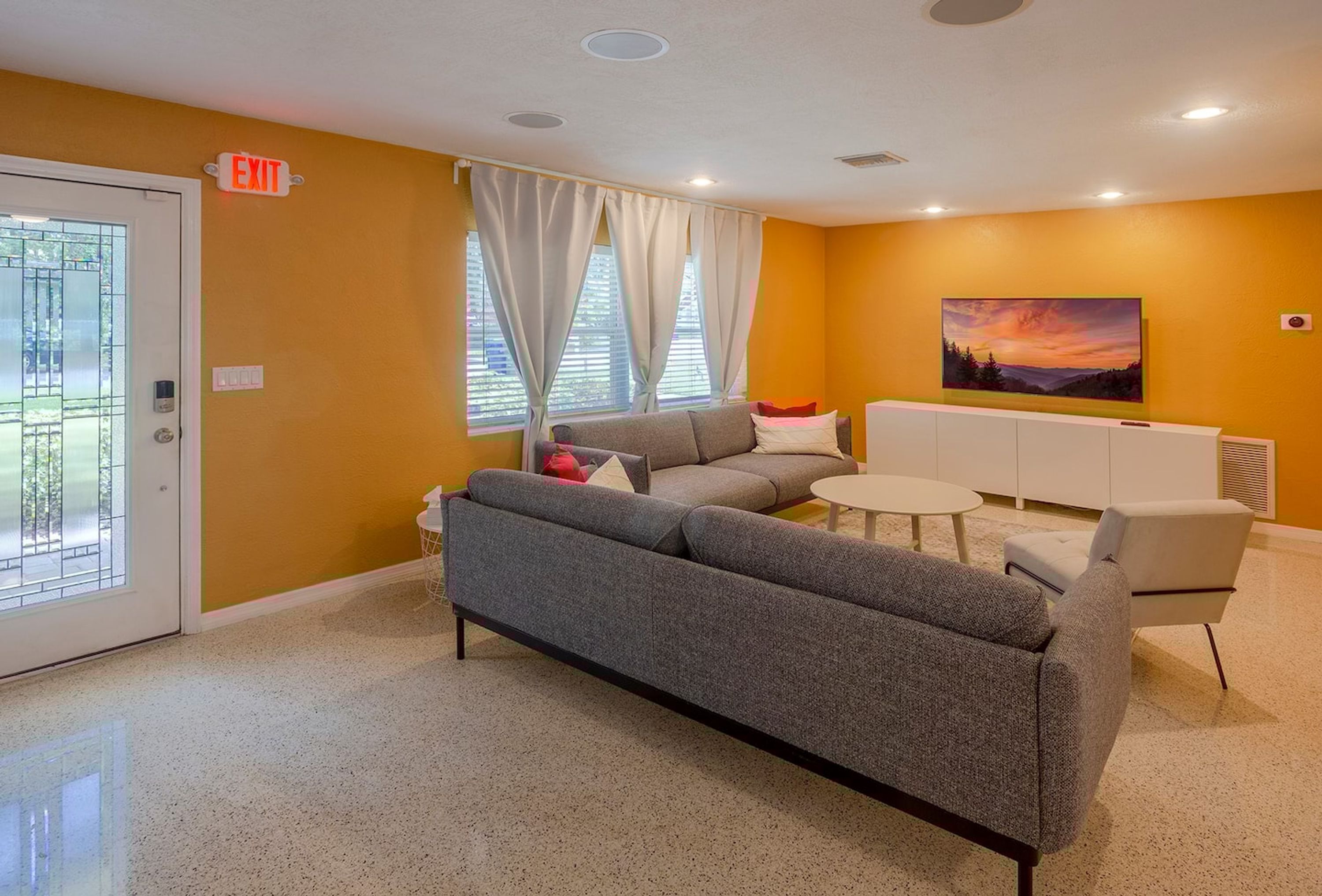 A modern living room with a sofa, armchairs, a small table, and a painting on the wall.