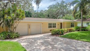 A single-story house with a garage, surrounded by well-maintained lawns and tropical plants. - Breathless Backyard Amazing Pool (Largo)