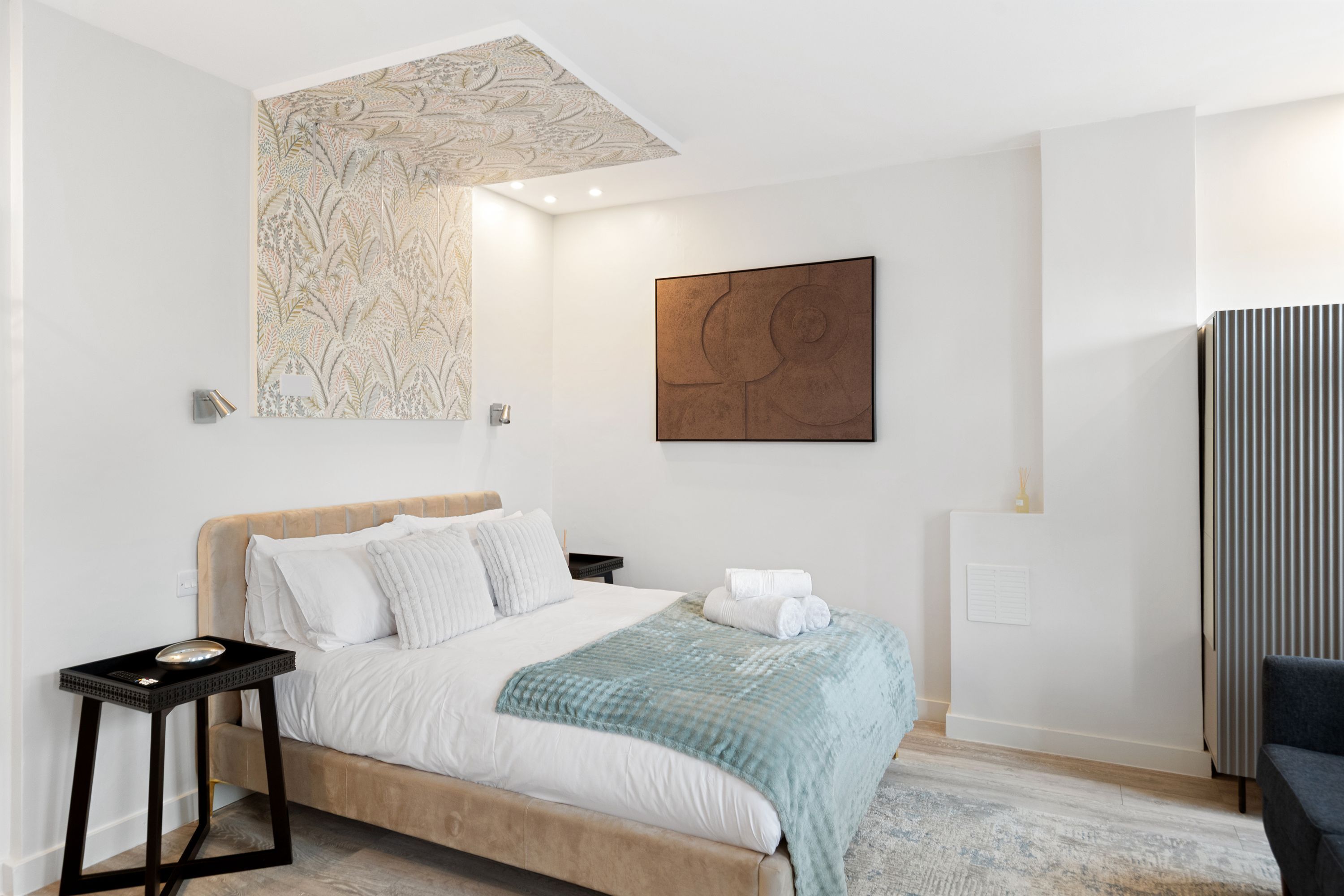 Une chambre à coucher moderne avec un lit, une table de chevet, une œuvre d’art murale et un radiateur.
