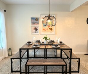 A dining area with a wooden table and benches, framed artwork on the wall, and a hanging light fixture.