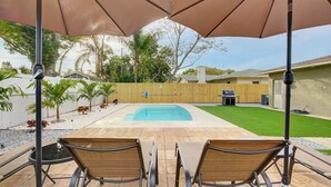 A backyard with a swimming pool, two lounge chairs, and a barbecue area.
