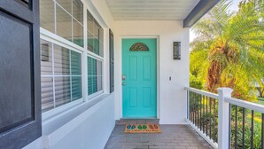 A turquoise door with a decorative arch, a white porch railing, and a doormat with a colorful design. - Light Sand With Heated Pool (Largo)