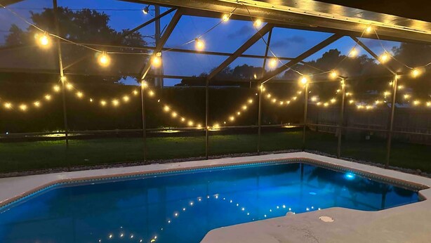 A swimming pool with string lights above, surrounded by a glass enclosure. - Light Sand With Heated Pool (Largo)