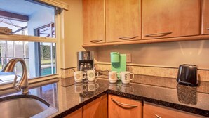 A kitchen with wooden cabinets, a granite countertop, and a coffee maker. - Light Sand With Heated Pool (Largo)