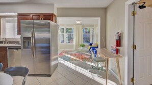 Una cocina con un refrigerador de acero inoxidable, armarios de madera, una mesa de comedor con sillas y vista a una sala de estar a través de una ventana.