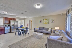 A modern kitchen with stainless steel appliances, a dining area with a round table and chairs, a gray sofa, and a patterned rug.