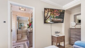 A bedroom with a bed, a bedside table, a dresser, a television mounted on the wall, and a door leading to another room. - Private Villa With Courtyard (Clearwater)