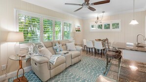 A living room with a beige sofa, a glass coffee table, a dining area with white chairs, and a kitchen with a granite countertop. - Private Villa With Courtyard (Clearwater)