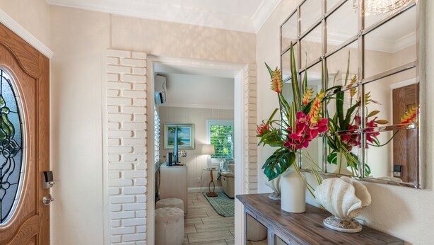 A hallway with a white brick wall, a wooden door with a glass window, and a console table with a decorative shell and flowers. - Private Villa With Courtyard (Clearwater)