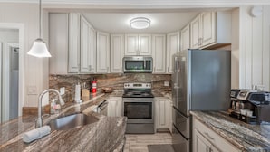 A modern kitchen with white cabinets, a granite countertop, stainless steel appliances, and a pendant light. - Private Villa With Courtyard (Clearwater)