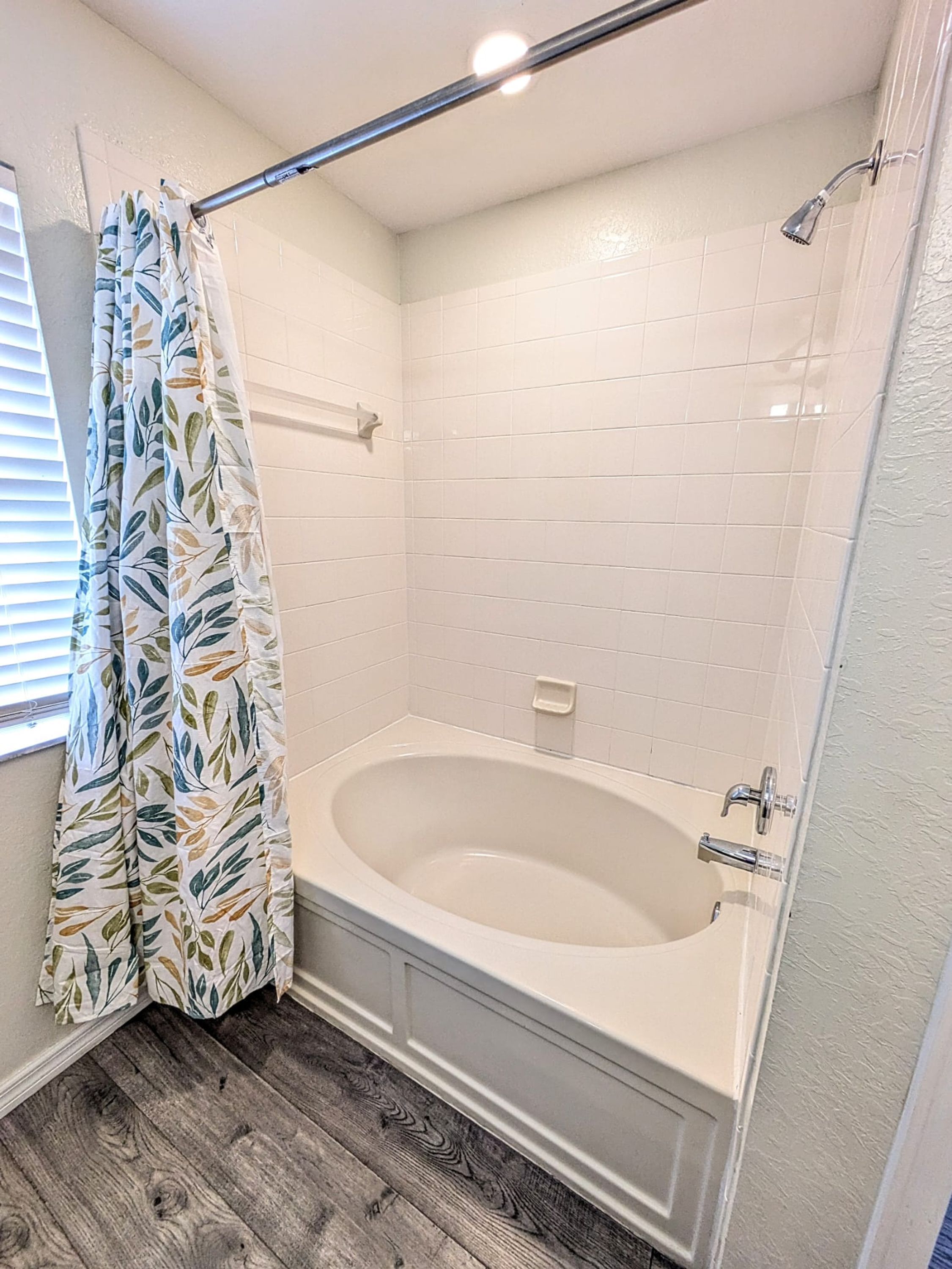 Une salle de bain avec une baignoire, une douche et une fenêtre avec des stores.