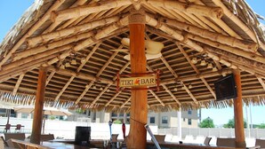 Een tiki bar met rieten dak en houten balken.
