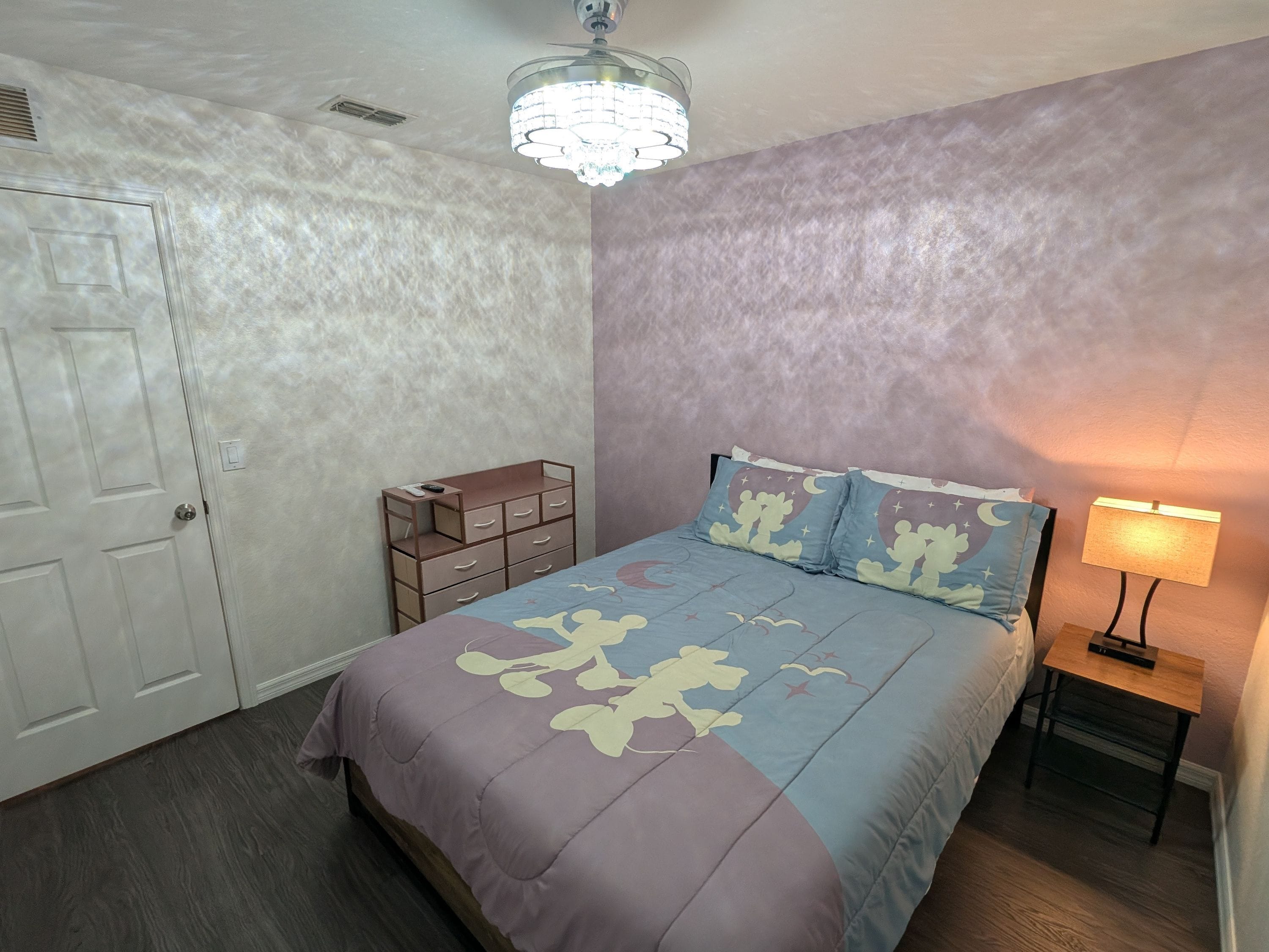 Een slaapkamer met een bed, nachtkastje, kapstok en plafondventilator.