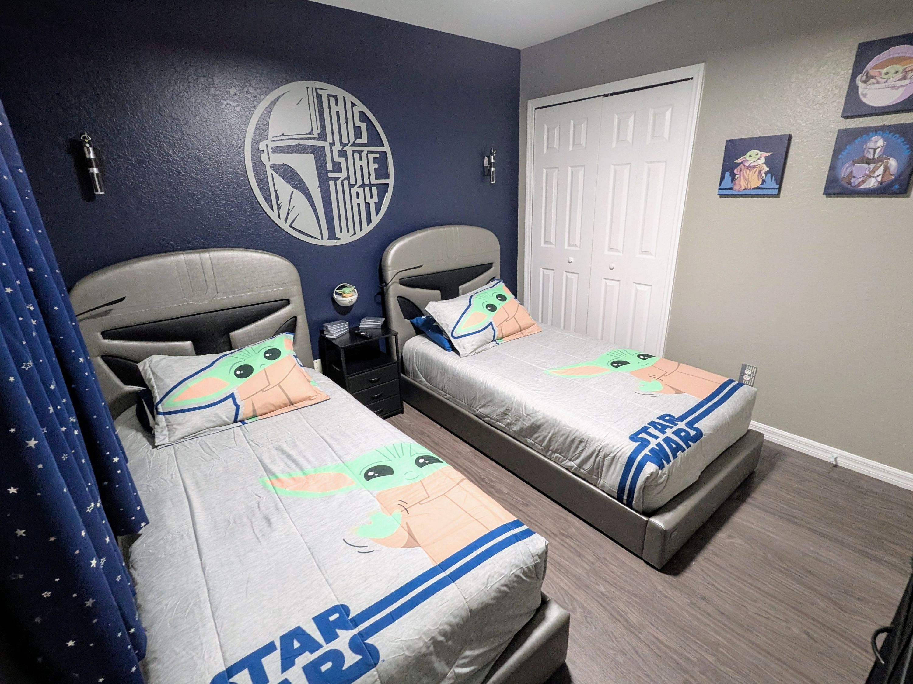 A bedroom with two beds, Star Wars themed bedding, a Star Wars wall decal, and a door with a Star Wars poster.