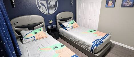 Un dormitorio con dos camas, ropa de cama con temática de Star Wars, un adhesivo mural de Star Wars y una puerta con un cartel de Star Wars.