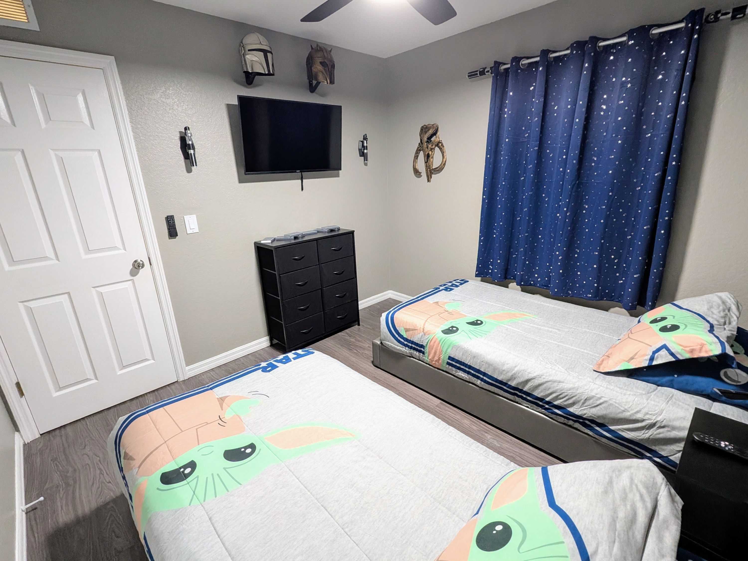 A bedroom with two beds, a TV, a dresser, and Star Wars-themed decor.