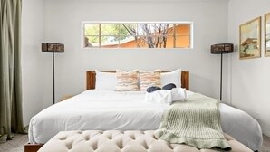 Une chambre à coucher bien aménagée, avec un grand lit, une table de chevet, une fenêtre donnant sur un beau paysage et deux lampadaires.