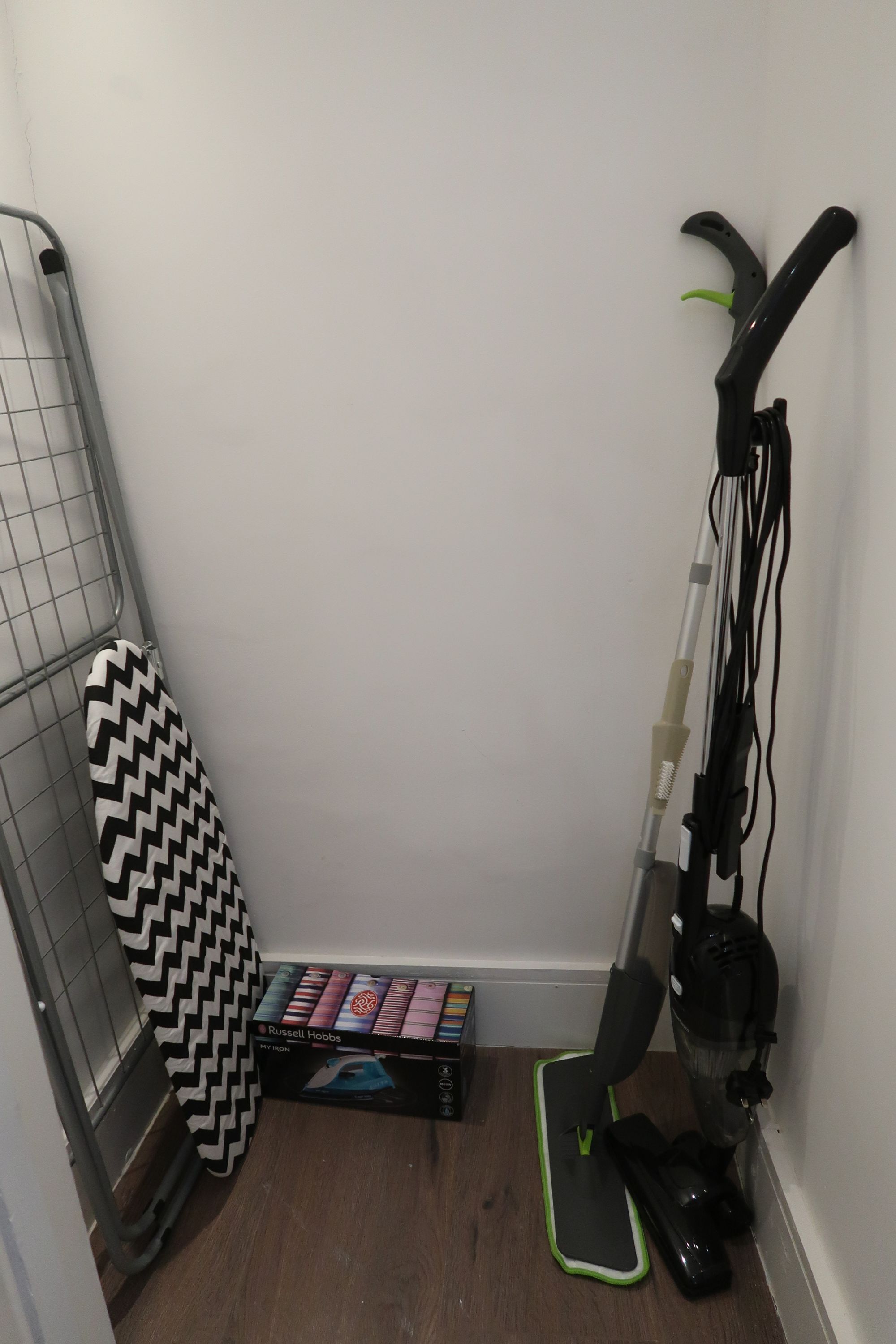 A corner of a room with a standing fan, a black and white iron, and a box of Russell Hobbs irons.