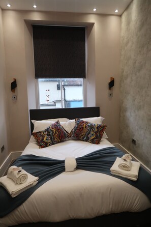 A neatly made bed with a black headboard, white and colorful patterned pillows, and a blue blanket. - Quaint Retreat in Sherborne s Historic District (Sherborne)