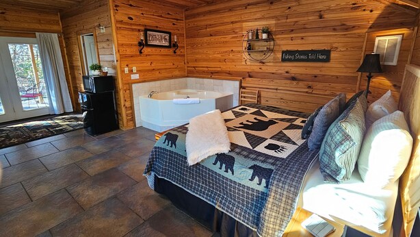 Une pièce aménagée dans le style d’un chalet en rondins, avec un grand lit, un coin salon, une cheminée, une baignoire et un panneau indiquant une zone de pêche.