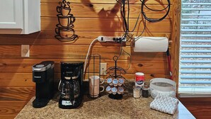 Une cuisine équipée d’un téléviseur fixé au mur, d’une machine à café, d’une cafetière, d’une tasse, d’un porte-tasse et d’un panier.