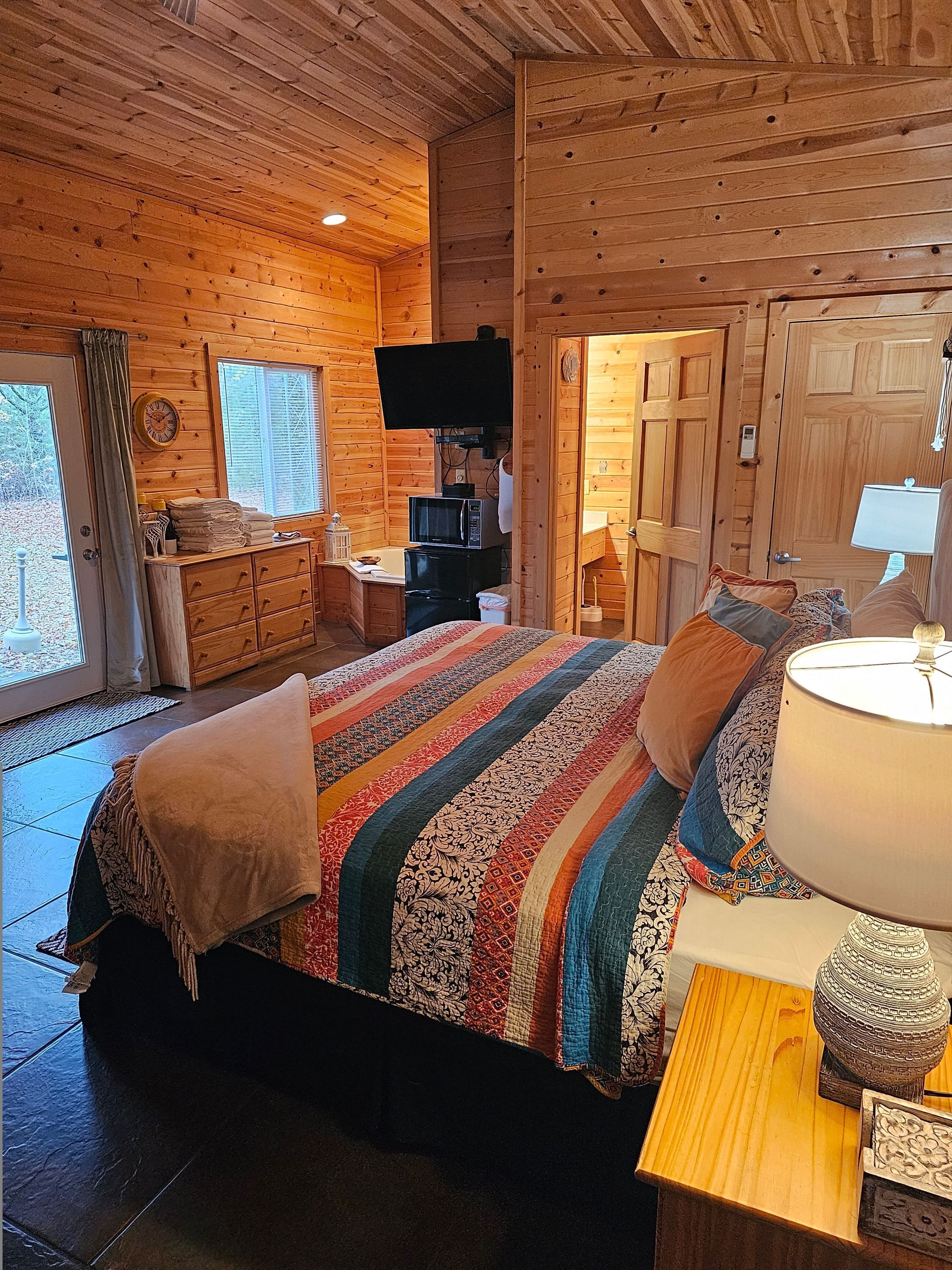 A wooden cabin bedroom with a bed, a TV, a desk, and a door.
