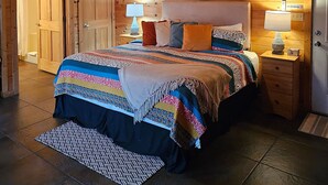 Un dormitorio con paneles de madera, una cama, mesitas de noche, un macramé colgante y un ventilador de techo.