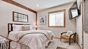 Un dormitorio con una cama grande, una silla, un televisor y una ventana.