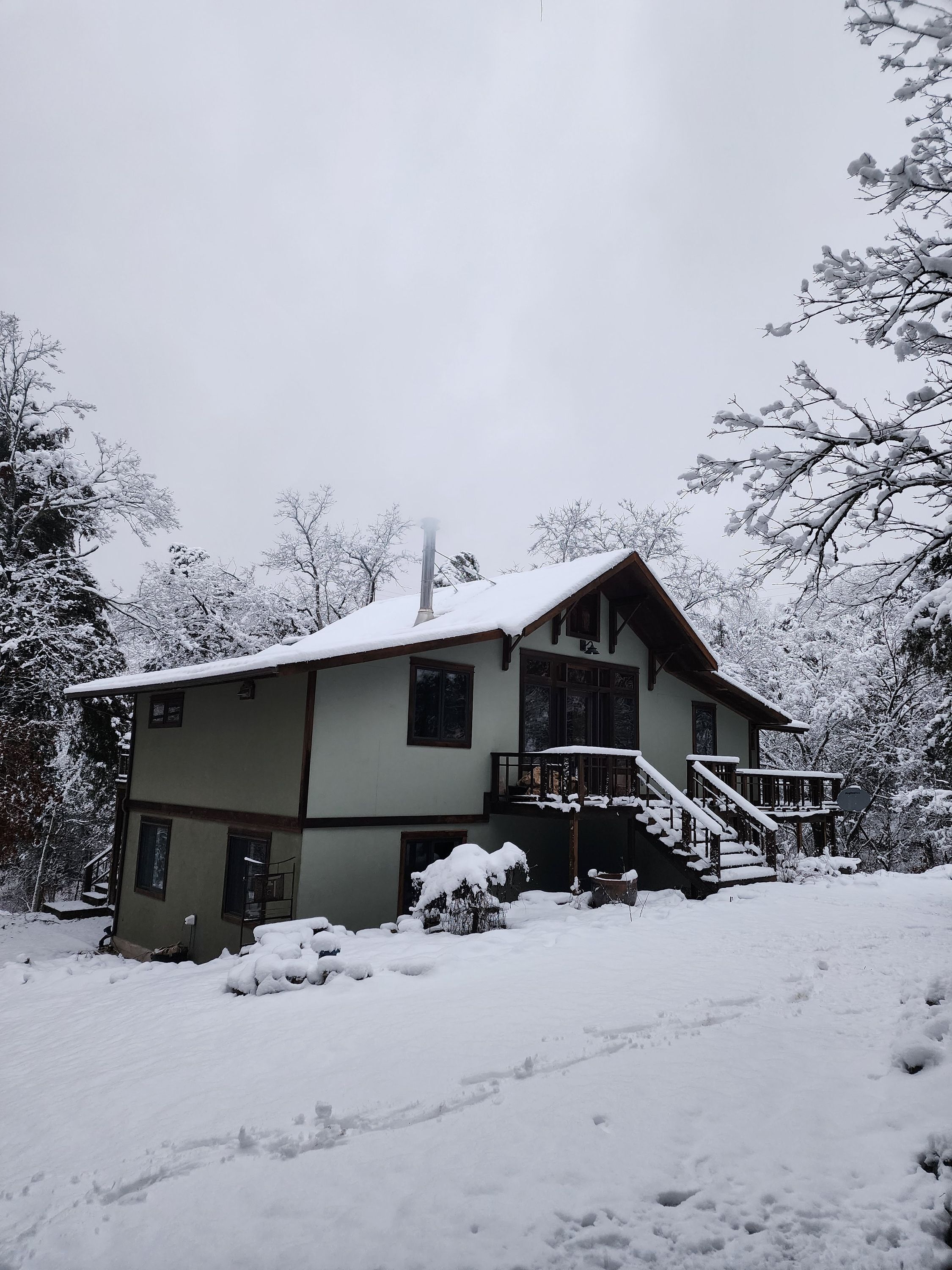 Una casa de dos pisos con un balcón y una chimenea, rodeada de árboles cubiertos de nieve.