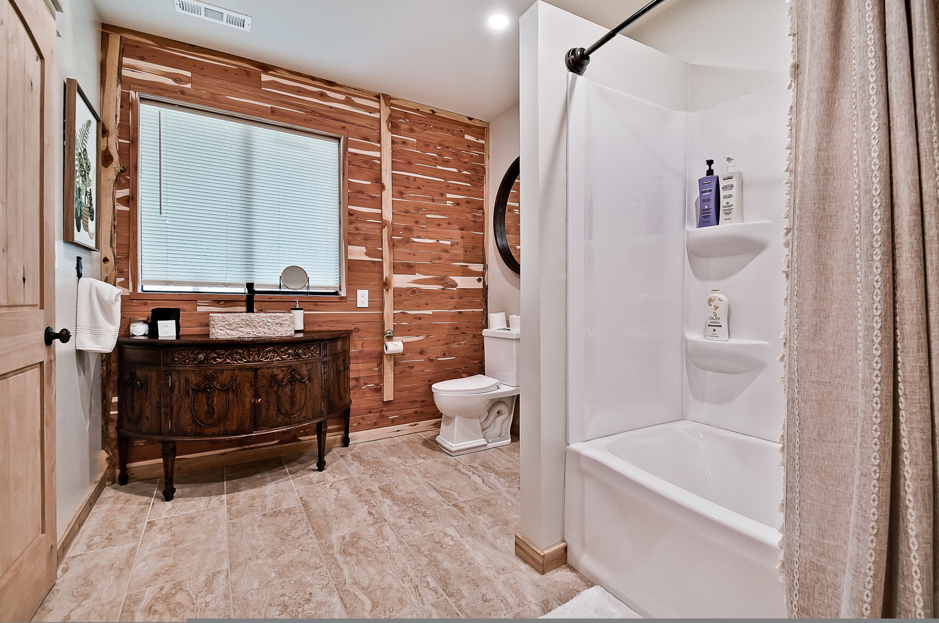 Une salle de bain avec un mur recouvert de lambris en bois, un meuble-lavabo avec un miroir, des toilettes et un espace douche doté d’étagères.