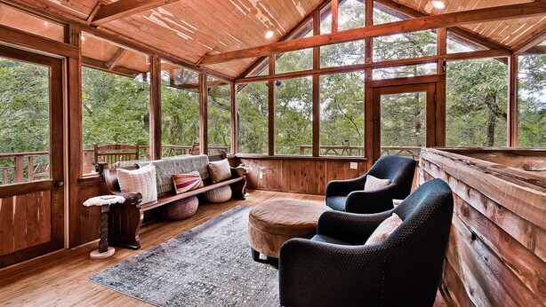 Interior de una cabaña de madera con un ventanal grande, un sofá, un sillón y una alfombra.