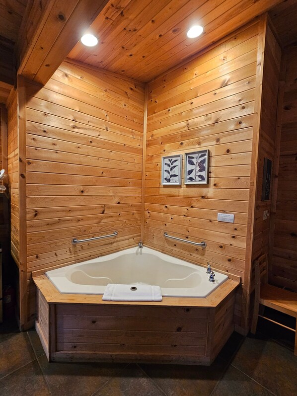 A wooden cabin with a large bathtub, wooden walls, and two framed pictures.