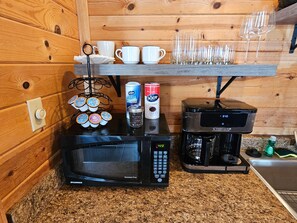 Una cocina con microondas, cafetera y varias cápsulas de café.