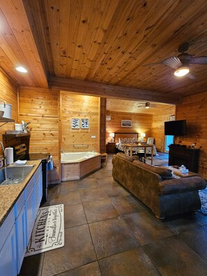 A cozy cabin interior with a wooden interior, a large bathtub, a sofa, and a television.