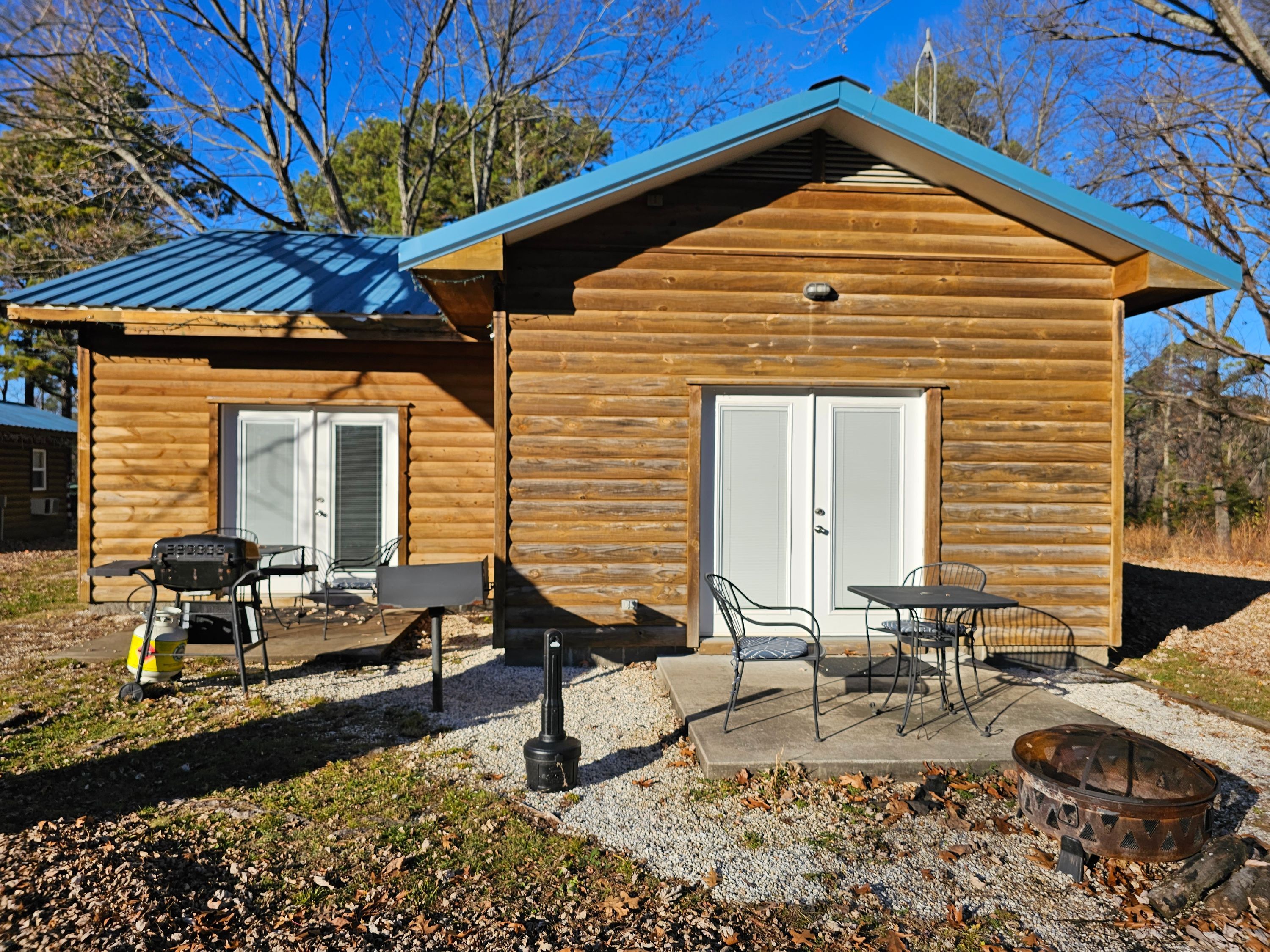Een houten chalet met een patio, inclusief een barbecue, stoelen en een vuurkuil.