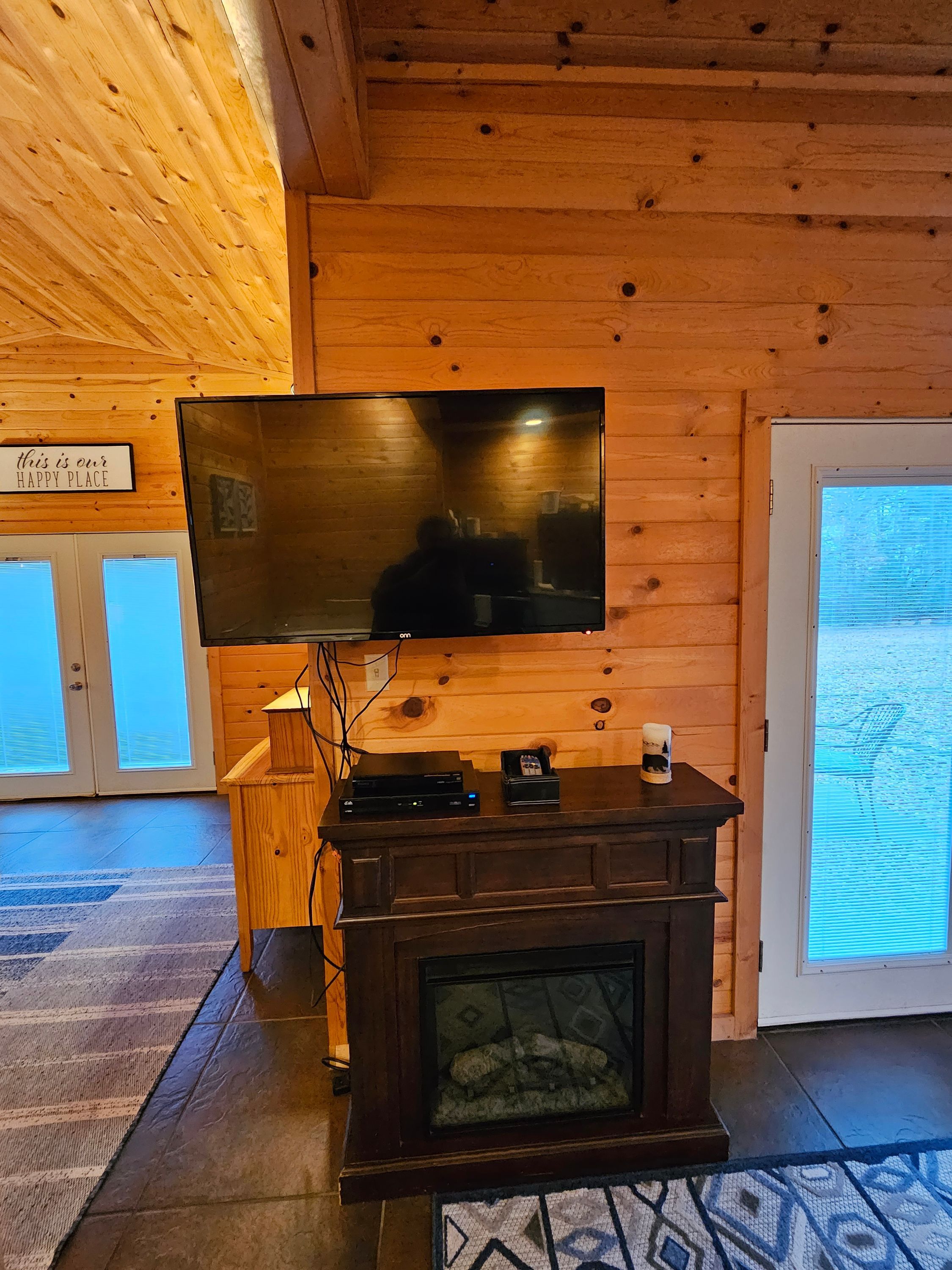 A wooden interior with a flat-screen TV mounted on a wall, a fireplace with a glass door, and a sign that reads "this is our happy place."