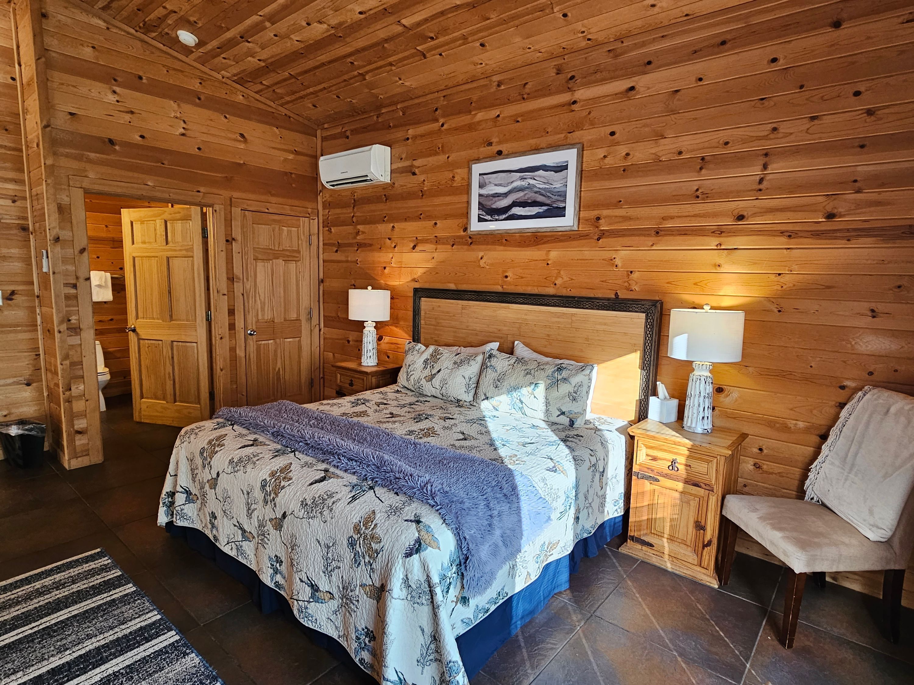 A wooden-paneled bedroom with a bed, two bedside tables, a chair, and a picture on the wall.