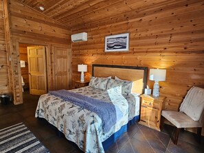 Un dormitorio con paneles de madera, una cama, dos mesitas de noche, una silla y un cuadro en la pared.