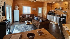 Interior acollidor d'una cabana amb zona d'estar, petita cuina i taula de menjador.