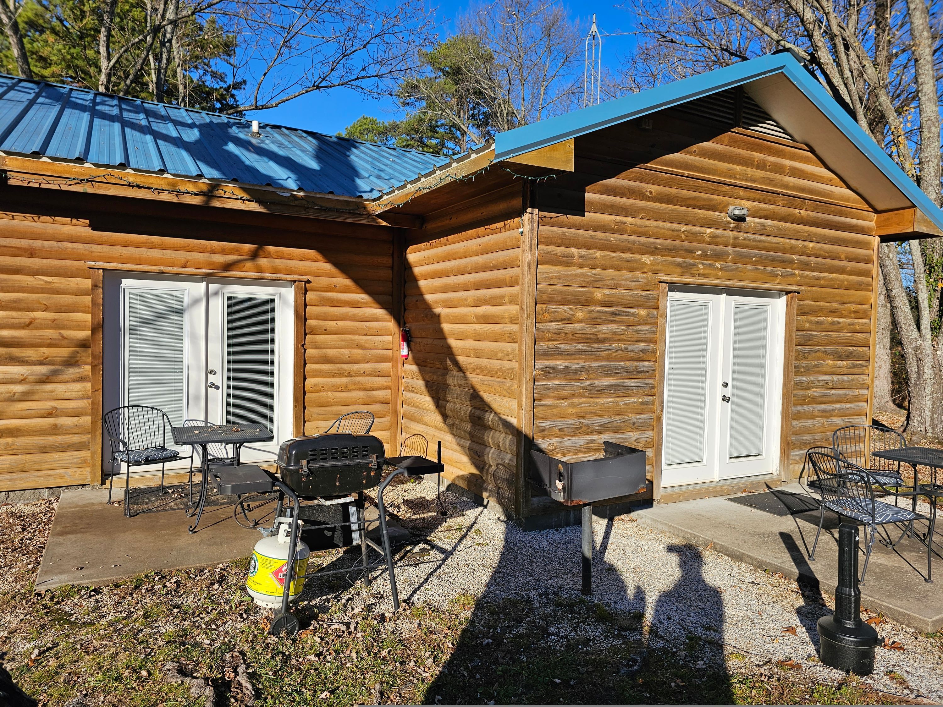 Eine Blockhütte mit zwei Türen, einer Terrasse mit Gartenmöbeln und einem Grill.